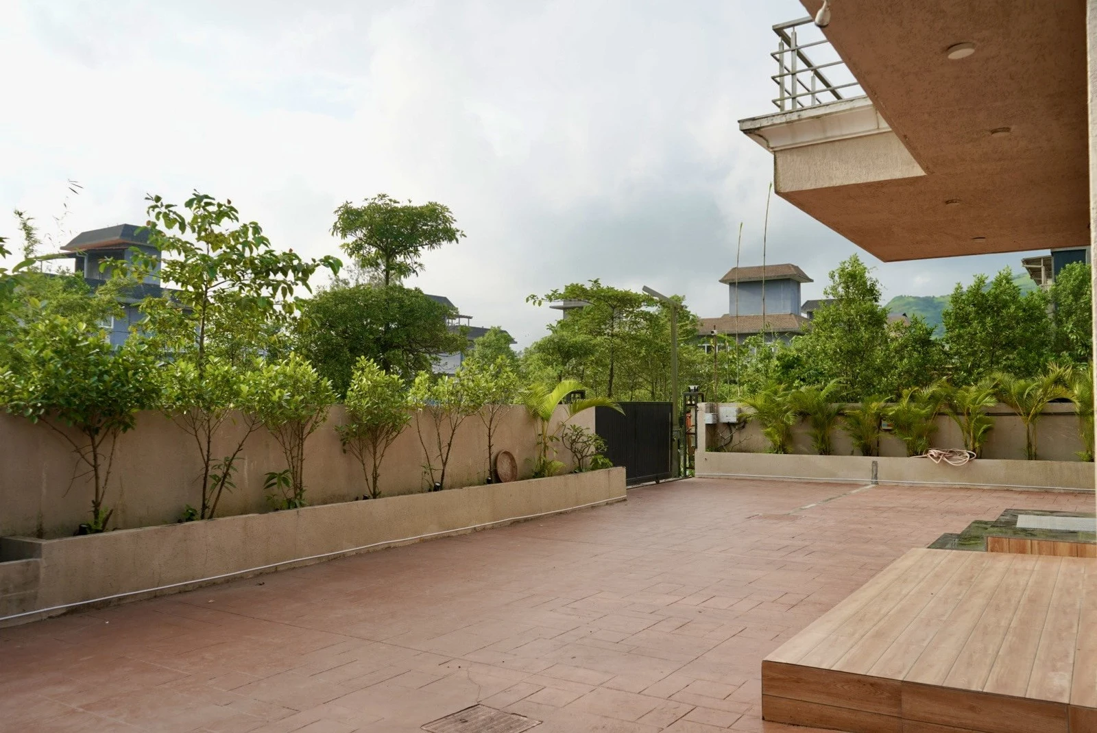 The villa’s open tiled courtyard in daylight, bordered by planters and green trees.
