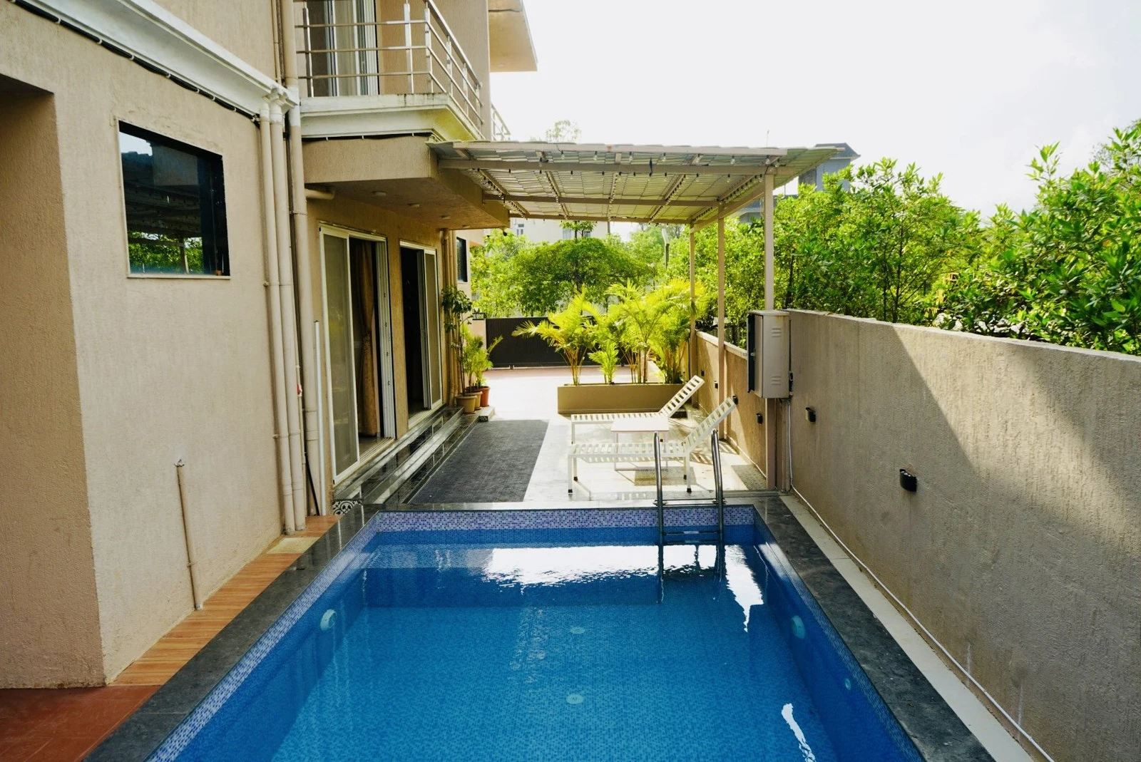 A view along the full length of the blue private pool, with the villa on one side and white loungers beneath the covered deck at the far end.